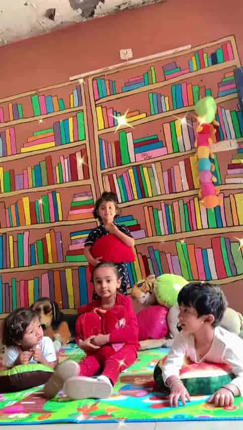 Children reading on mats in front of a painted book wall